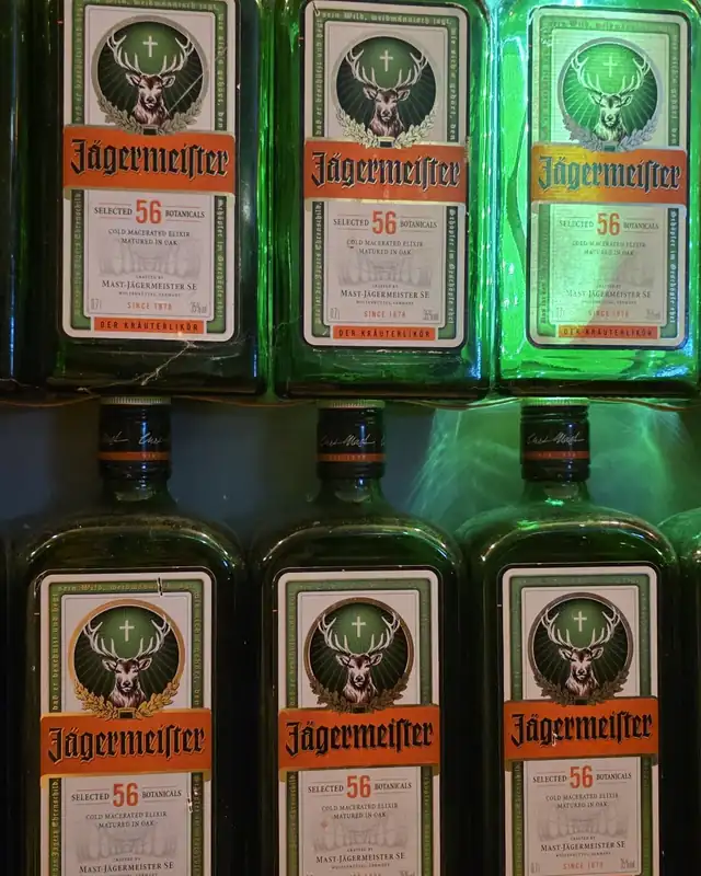 Butelki Jägermeistera ustawione na półkach z zielonym światłem