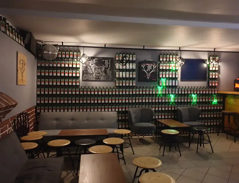Sala z sofami i okrągłymi stołkami, za nimi ściana butelek Jägermeistera i logo z jeleniem