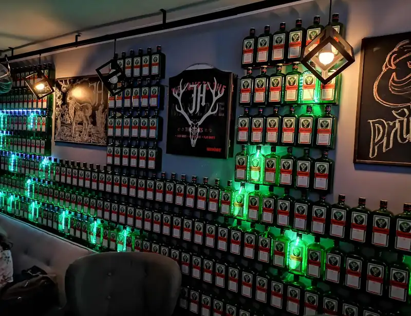 Podświetlona na zielono ściana z butelkami i logo Jager House
